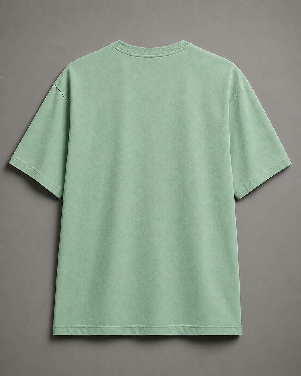 A light sage green short-sleeve t-shirt shown from the back, laid flat against a neutral gray background.