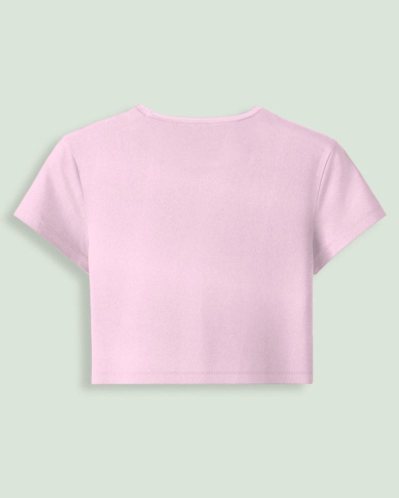 A light pink short-sleeve crop top shown from the back, centered on a solid pale green background.