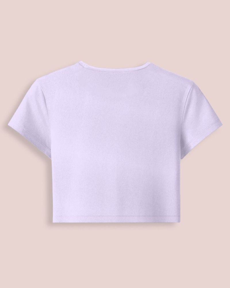 A light lavender short-sleeve crop top shown from the back, laid flat against a solid pale peach-beige background.