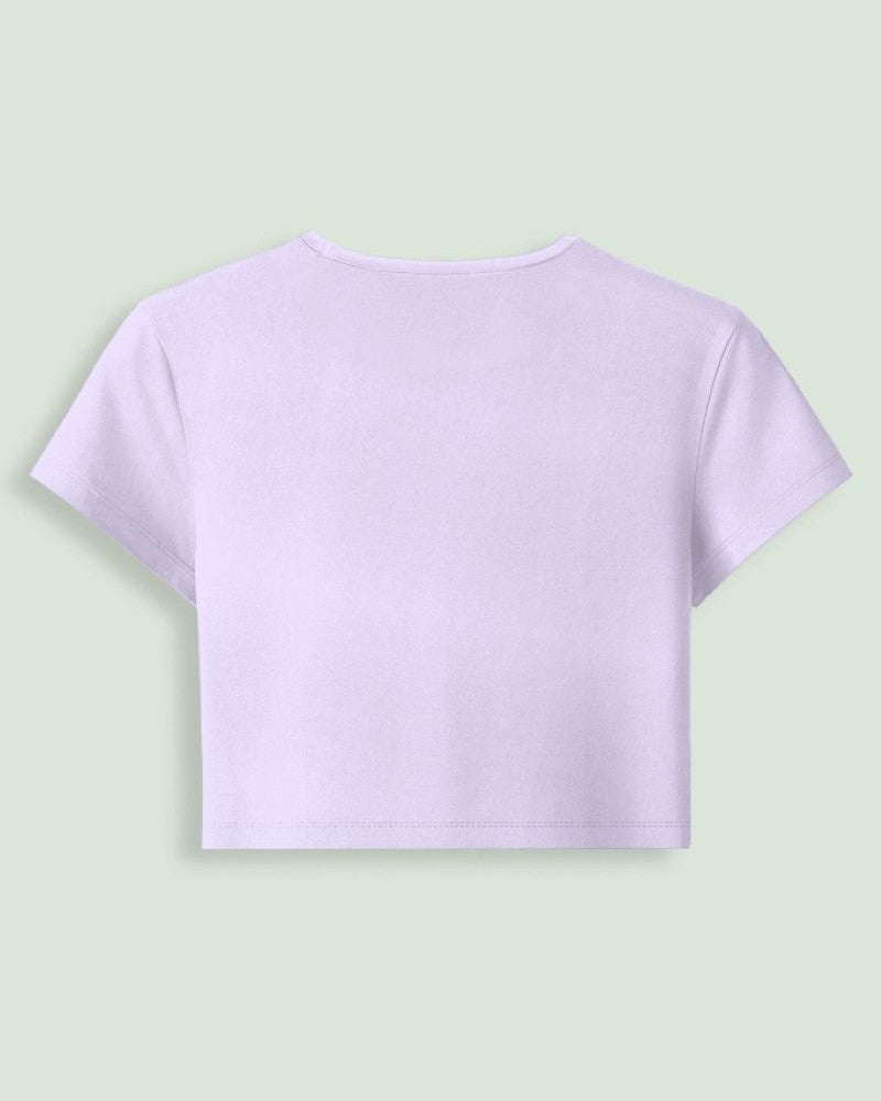 A light lavender short-sleeve crop top shown from the back, centered on a pale sage green background.