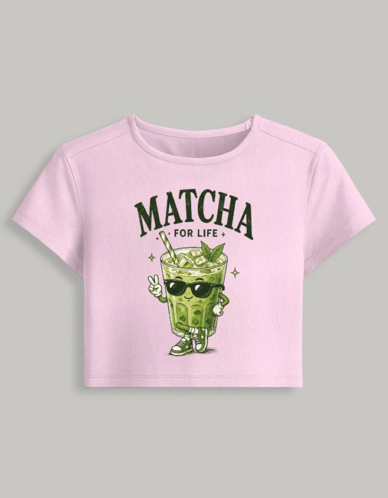 A light pink short-sleeve crop top featuring a cartoon matcha drink character wearing sunglasses under the text 'MATCHA FOR LIFE', displayed on a neutral gray background.