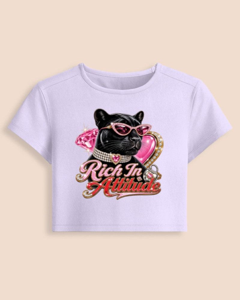 A light lavender short-sleeve crop top featuring a graphic of a black French bulldog wearing pink sunglasses and a pink bow, with the text 'Rich In Attitude' in pink and gold script.