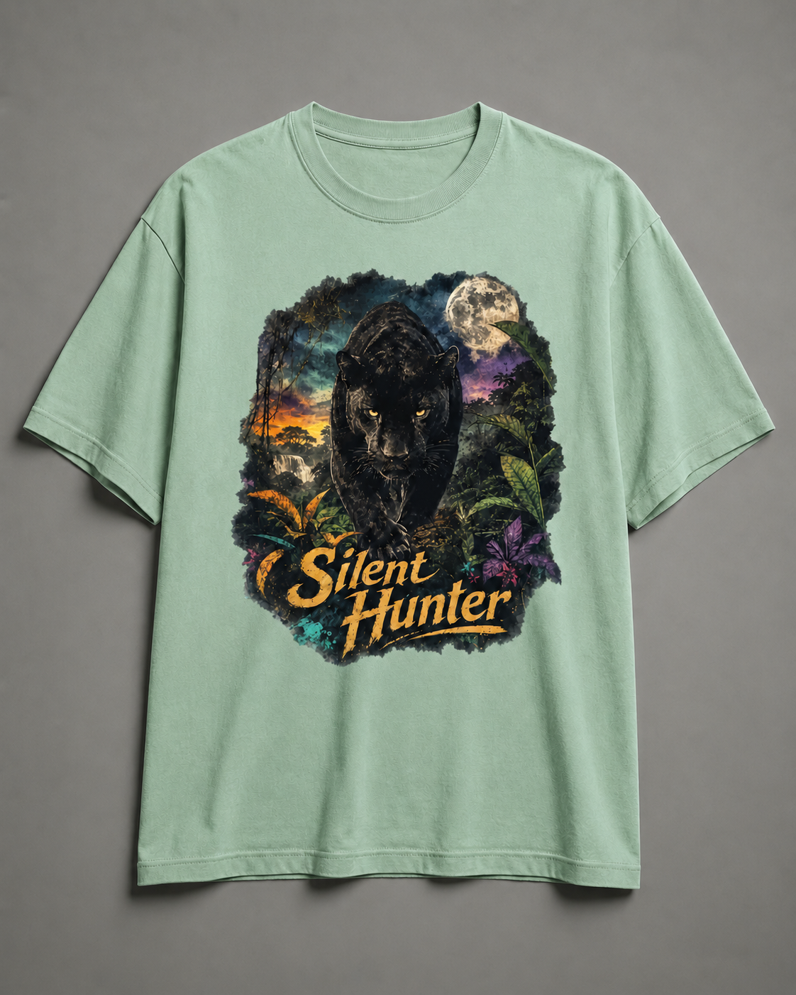 A light sage green short-sleeve t-shirt with a large graphic print on the front featuring a black panther, a full moon, and the text 'Silent Hunter' in yellow, displayed against a neutral gray background.