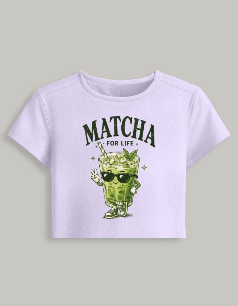 A light lavender short-sleeve crop top featuring a green cartoon matcha drink character wearing sunglasses and the text 'MATCHA FOR LIFE' printed on the front, displayed against a solid gray background.