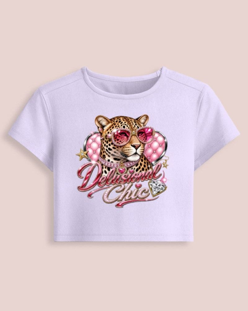 A light lavender short-sleeve crop top featuring a graphic of a leopard wearing pink sunglasses and a pink polka-dot collar, with the text 'Delicious Chic' in pink script below.