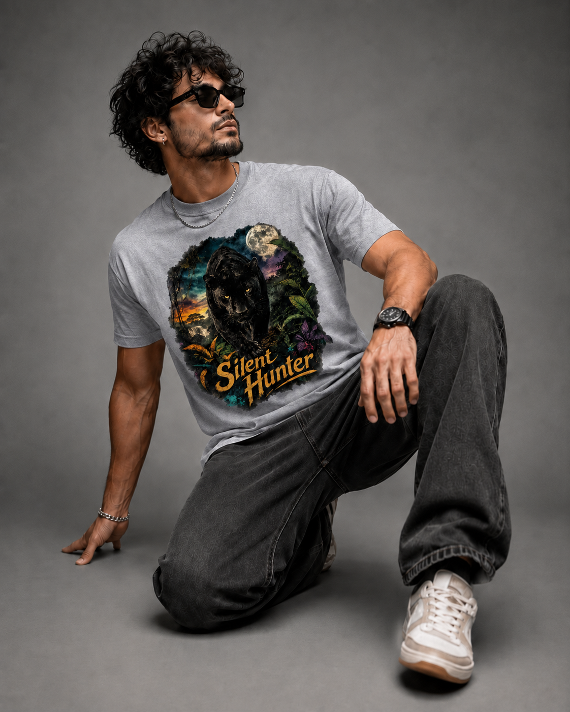 A man wearing a gray graphic t-shirt with a 'Silent Hunter' wolf design, dark gray jeans, and white sneakers, posing on a gray studio background.