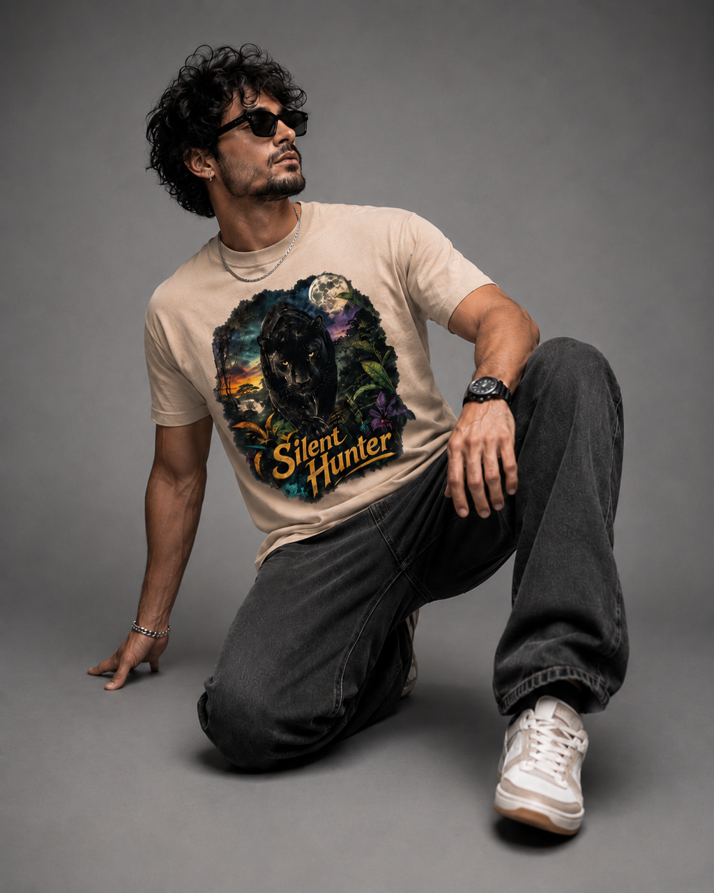A man wearing a beige graphic t-shirt with a 'Silent Hunter' wolf design, dark gray jeans, and white sneakers, posing on a solid gray studio background.