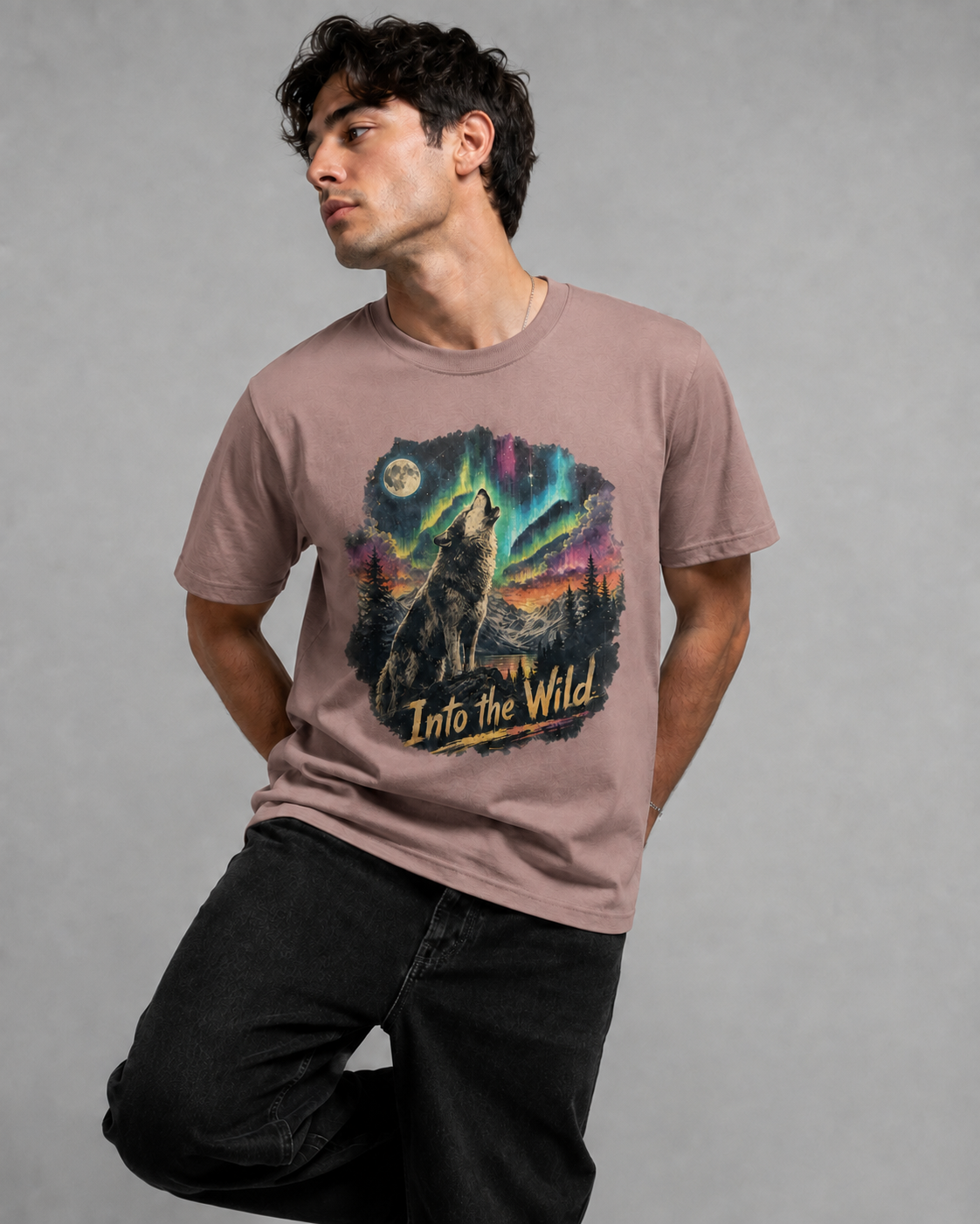 A man wearing a dusty rose short-sleeve t-shirt with a colorful graphic of a howling wolf under the aurora borealis and the text 'Into the Wild'.