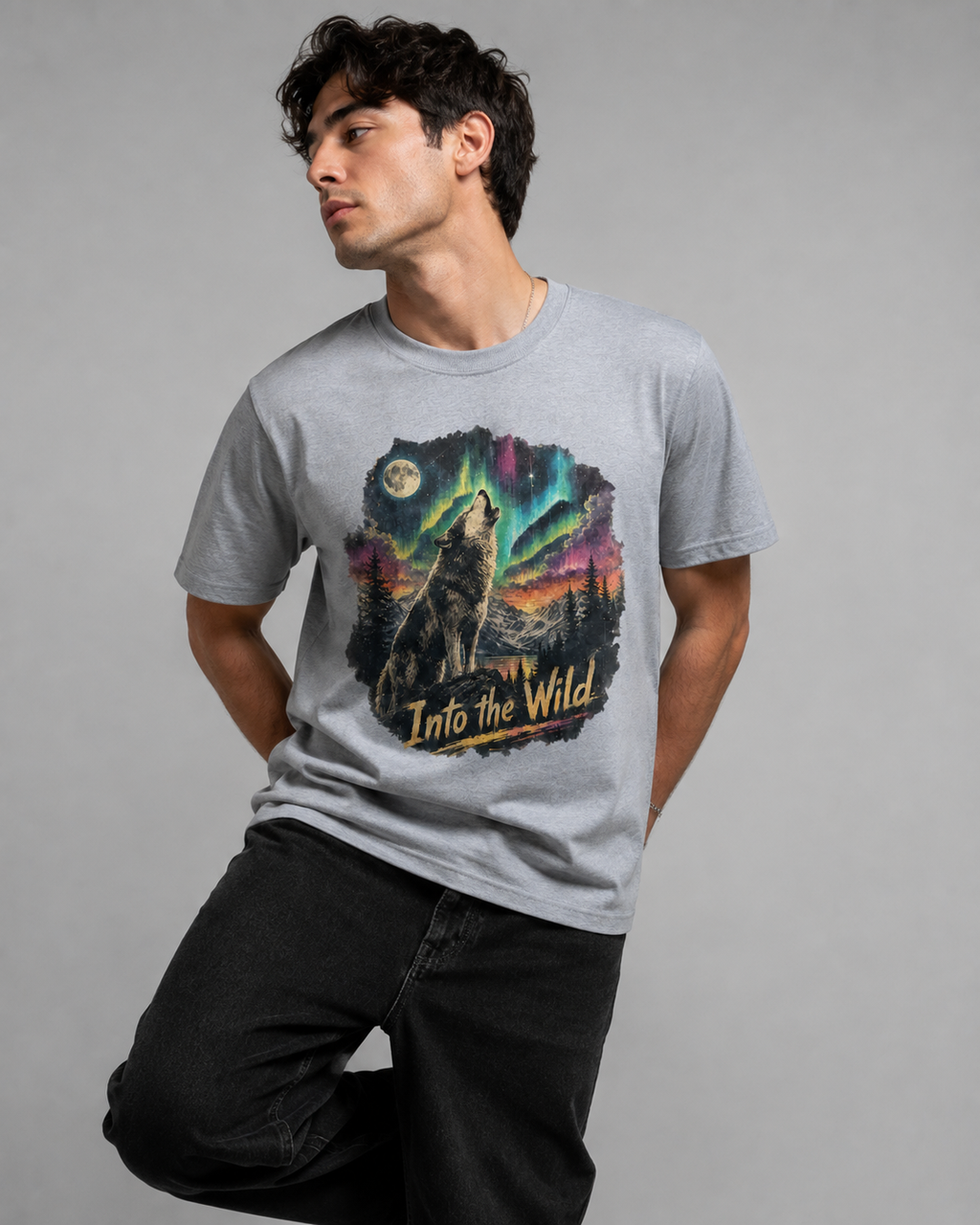 A man wearing a light gray crewneck t-shirt with a colorful graphic of a howling wolf under the aurora borealis and the text 'Into the Wild'.
