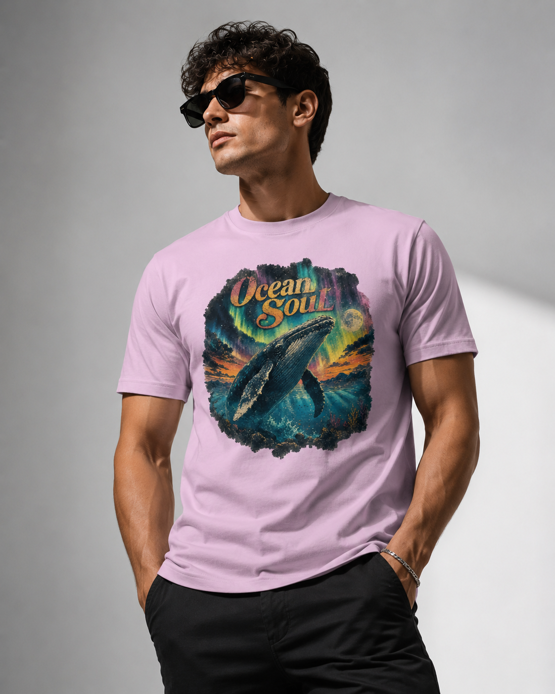 A man wearing a light purple t-shirt with a colorful graphic of a whale and the text 'Ocean Soul' on the front, paired with black pants and sunglasses, set against a gray studio background.