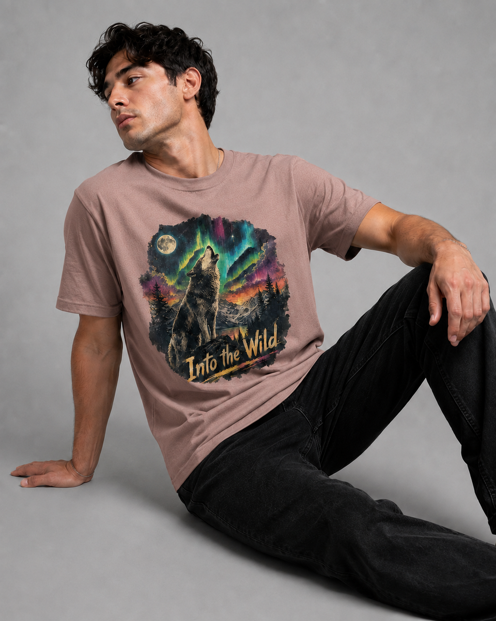 A man wearing a dusty rose graphic t-shirt with a wolf howling under the aurora borealis and the text 'Into the Wild'.