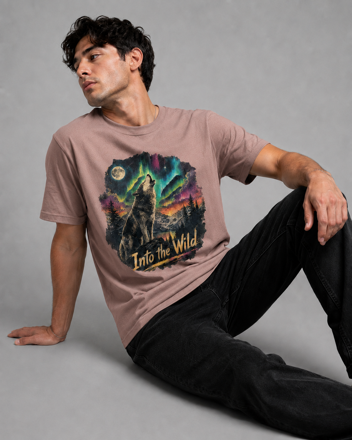 A man wearing a dusty rose graphic t-shirt with a wolf howling under the aurora borealis and the text 'Into the Wild'.